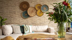 A living room with a wooden coffee table, a sofa with decorative pillows, a wall with woven baskets, and a vase with flowers. - El reloj casa hotel (Filandia)