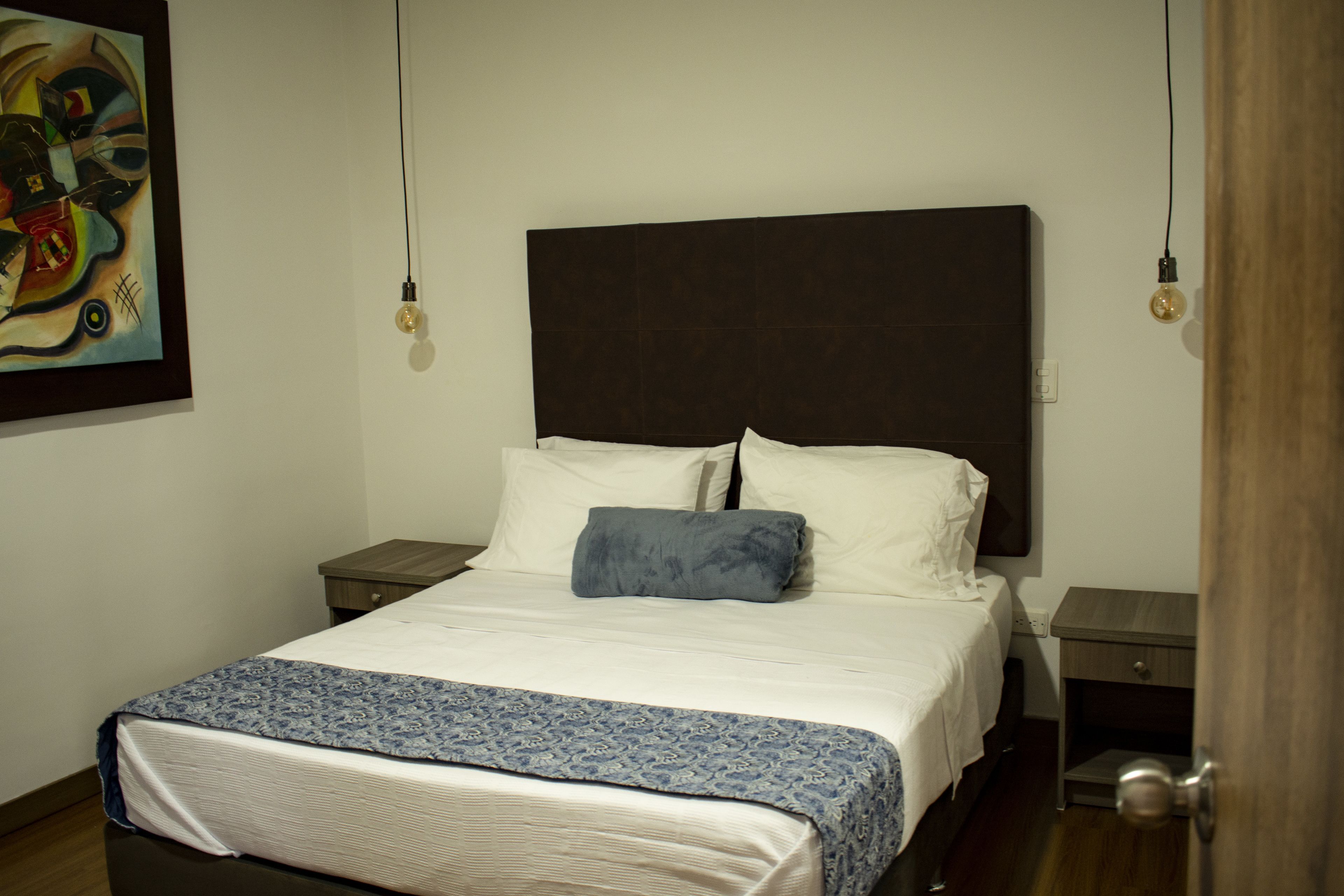 A neatly made bed with a patterned bedspread, a large headboard, and bedside tables with lamps.