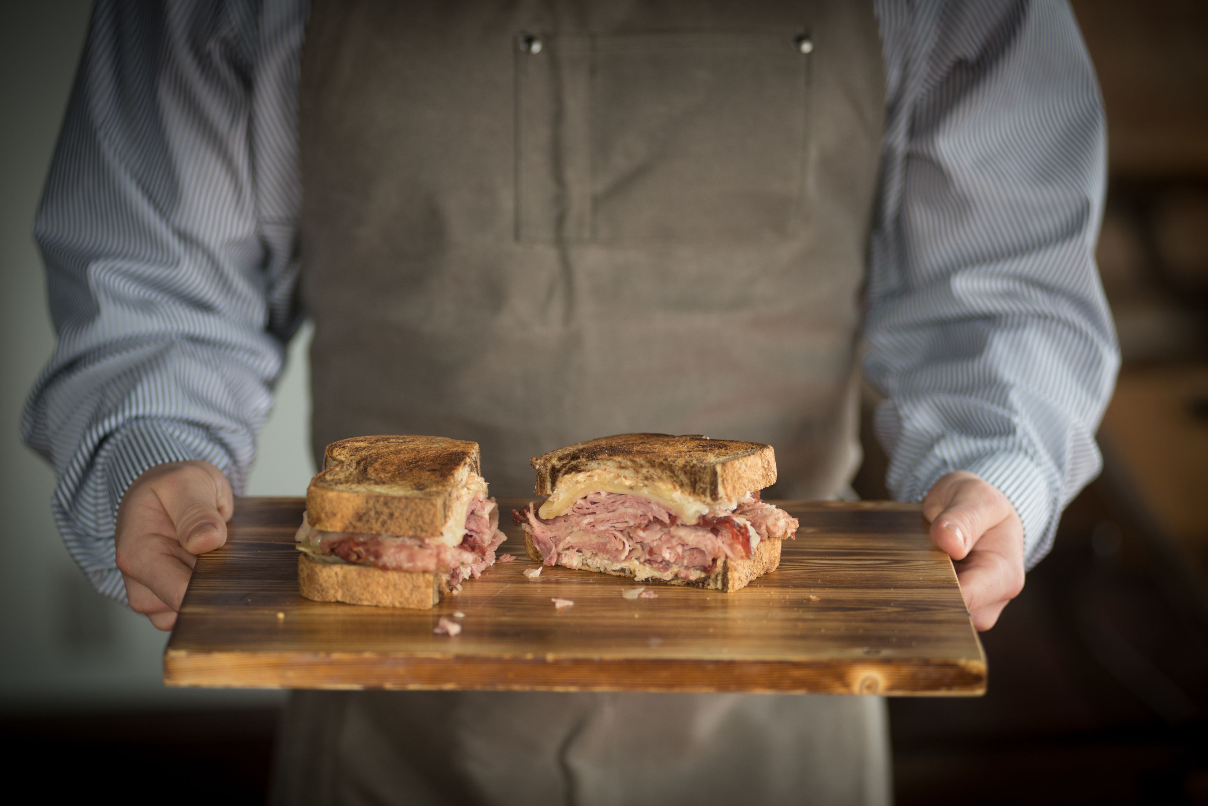 A person holding a wooden board with a sandwich cut in half.