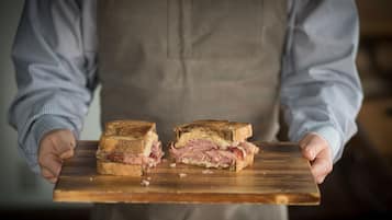 A person holding a wooden board with a sandwich cut in half.