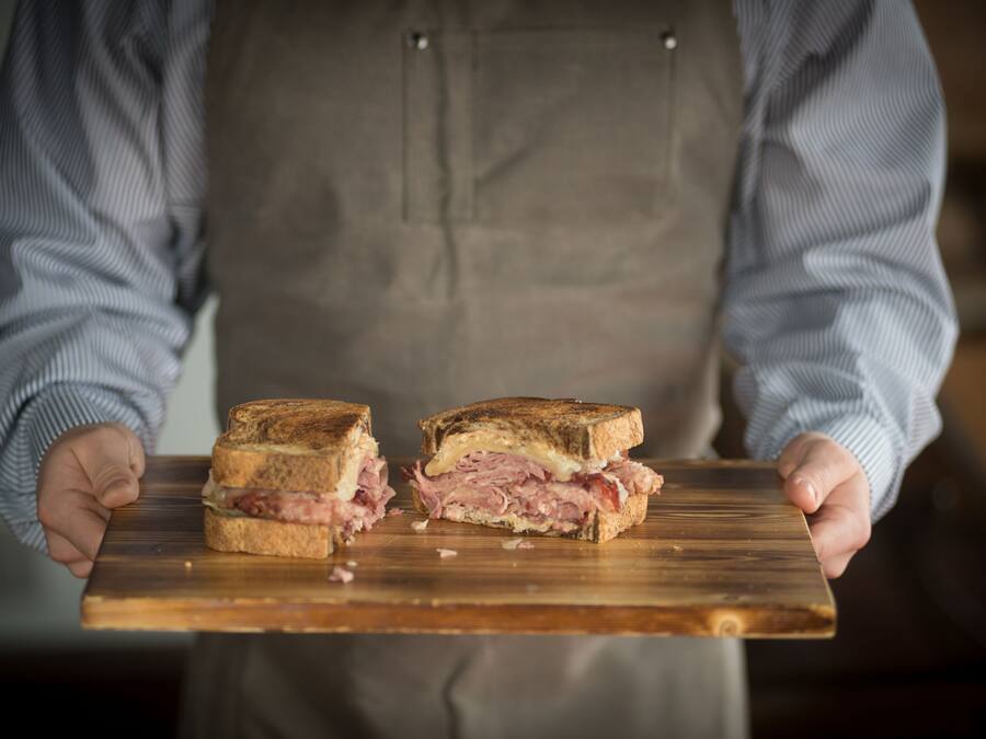 A person holding a wooden board with a sandwich cut in half.