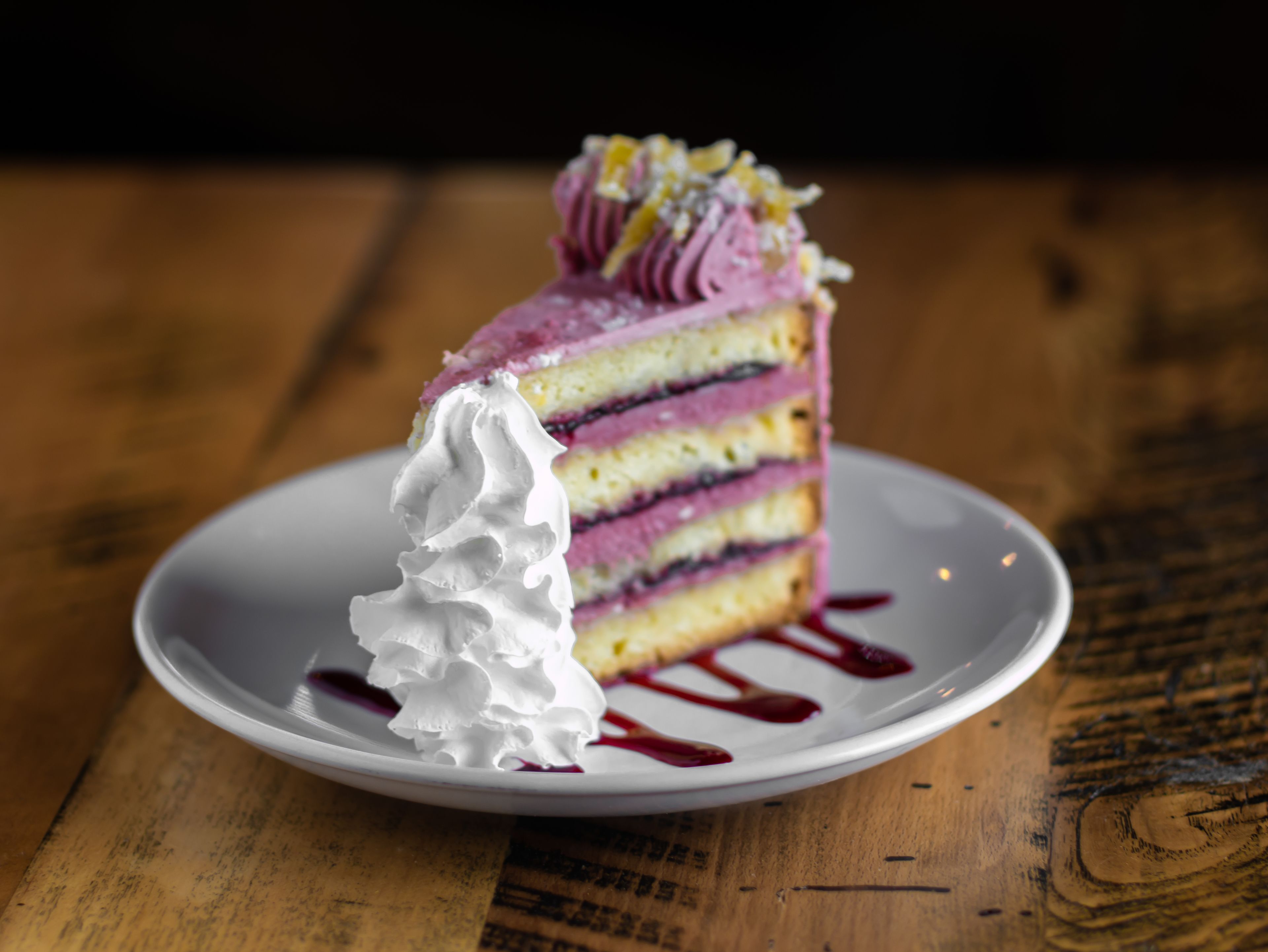 Una rebanada de pastel con crema batida y un hilo de jarabe rojo sobre un plato blanco.