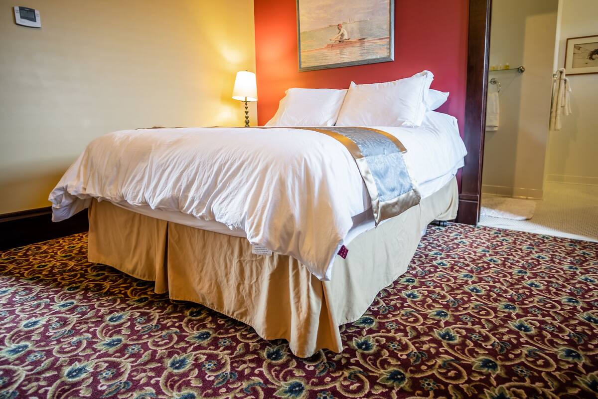 A hotel room with a bed, a lamp, a painting, and a shower area.