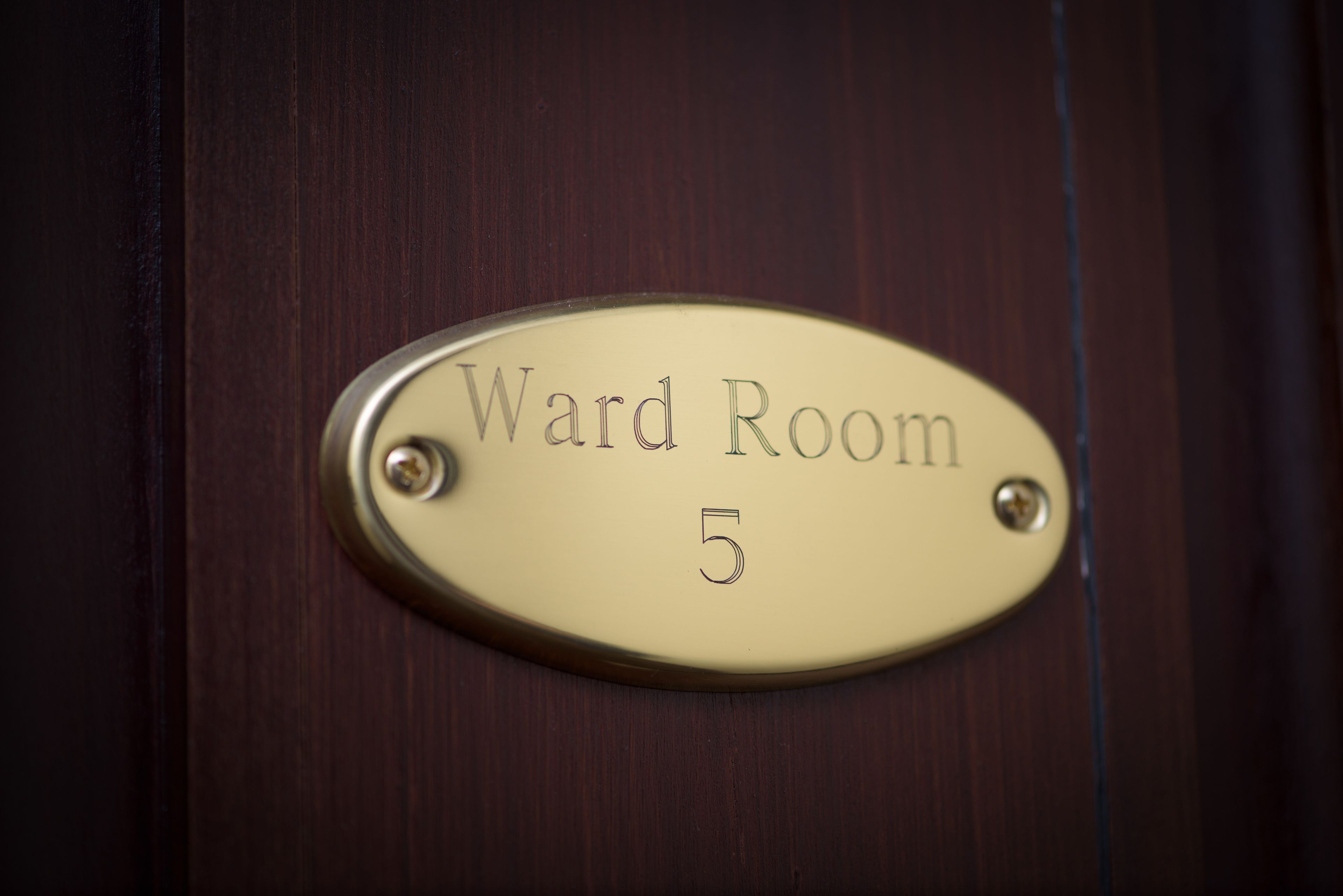 Una placa de bronce en una puerta de madera que indica 'Ward Room 5'.