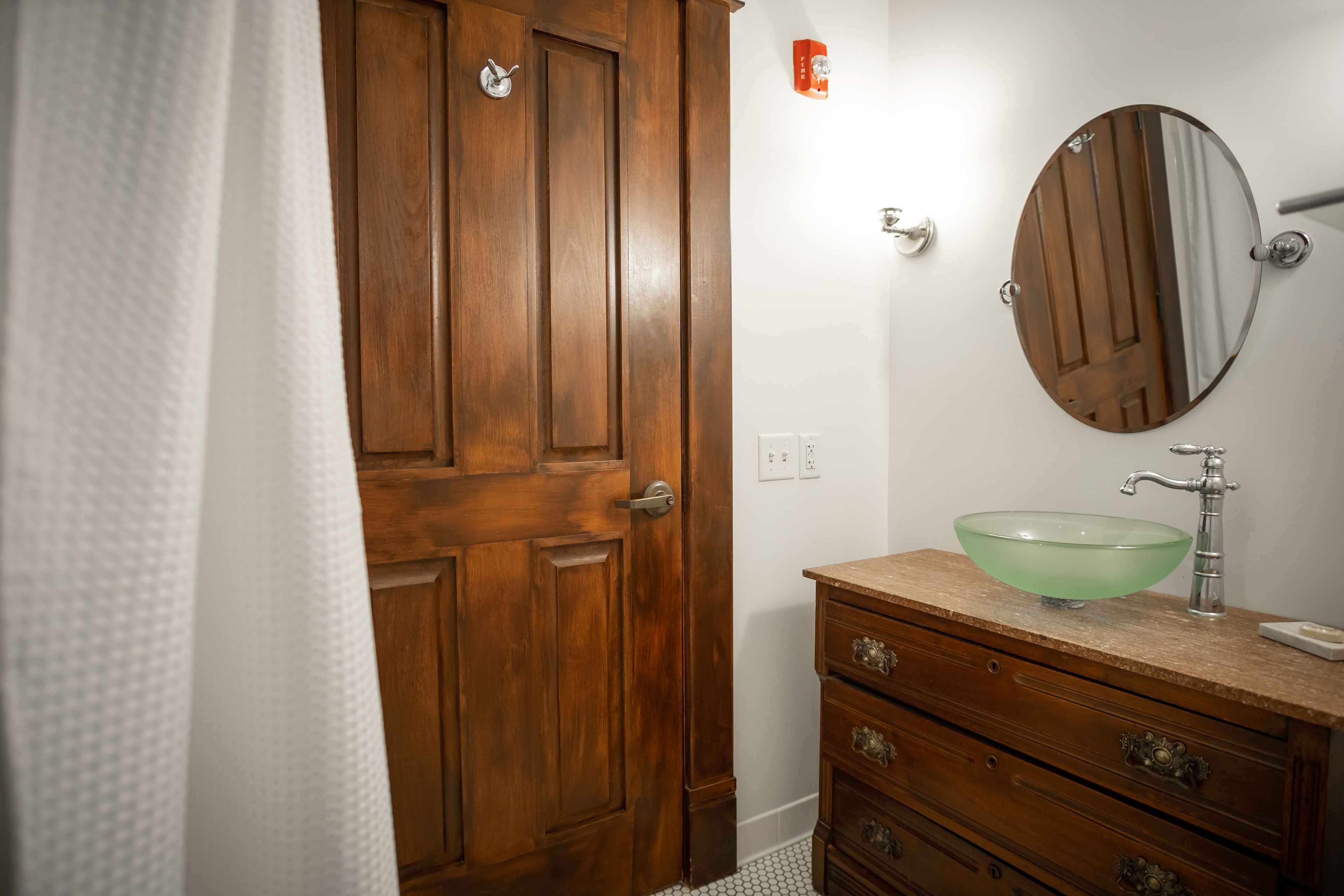 A bathroom with a wooden door, a glass sink, and a mirror.