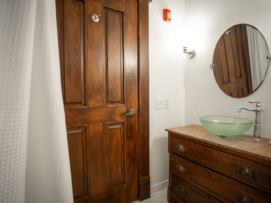 A bathroom with a wooden door, a glass sink, and a mirror.