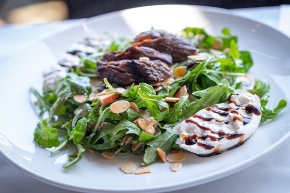 Un plato blanco con ensalada, que incluye hojas verdes, nueces y una cucharada de salsa blanca con un chorrito oscuro.