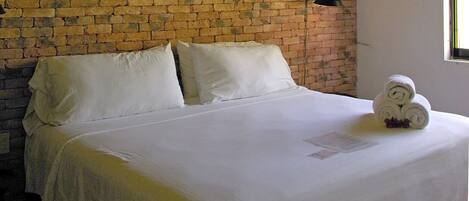 A neatly made bed with white linens, a brick wall background, and a small towel arrangement on the bed.