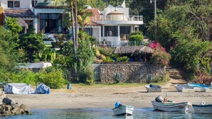 Une propriété située sur la côte, dotée d’un mur en pierre, d’une construction à toit de chaume et de plusieurs bateaux sur la plage.