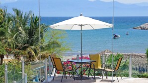 Une terrasse avec une table et des chaises, donnant sur une plage avec vue sur la mer et les montagnes.