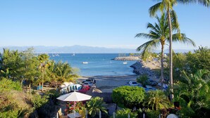 Une plage avec des palmiers, une côte rocheuse et des bateaux sur l’eau.