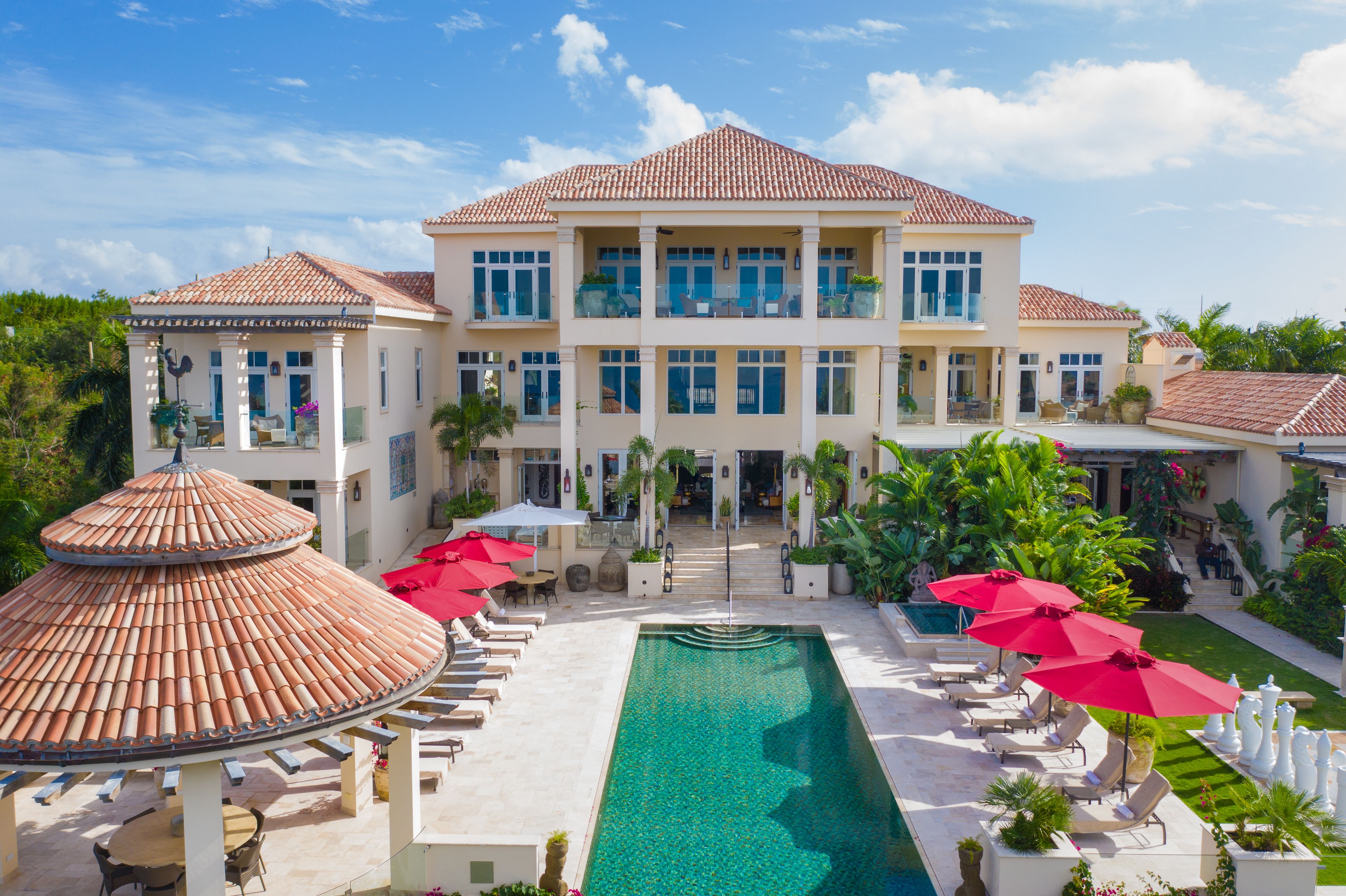 A large, two-story building with a swimming pool, outdoor seating, and a covered area with umbrellas.