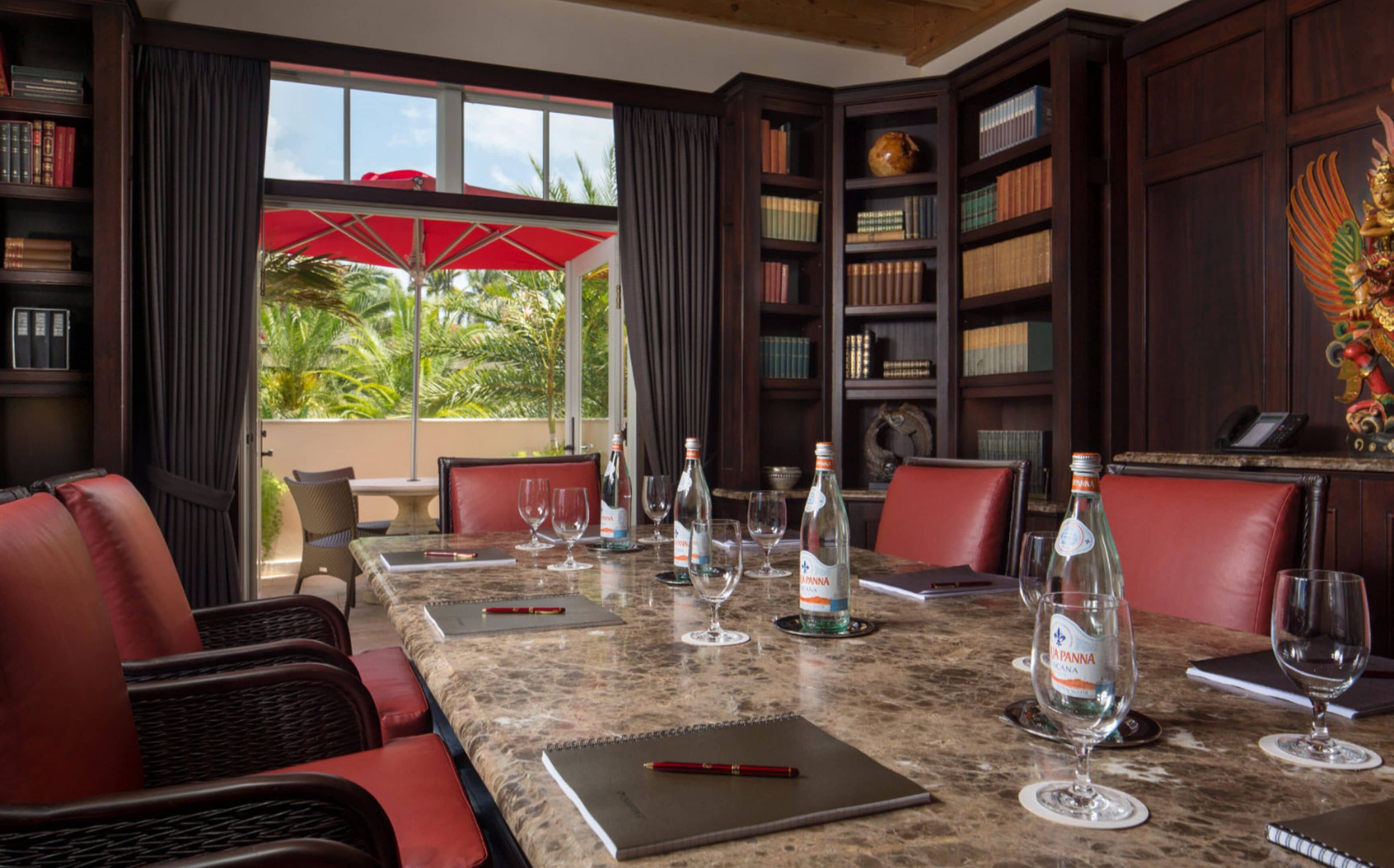 A conference room with a marble table, leather chairs, and a view of palm trees through large windows.