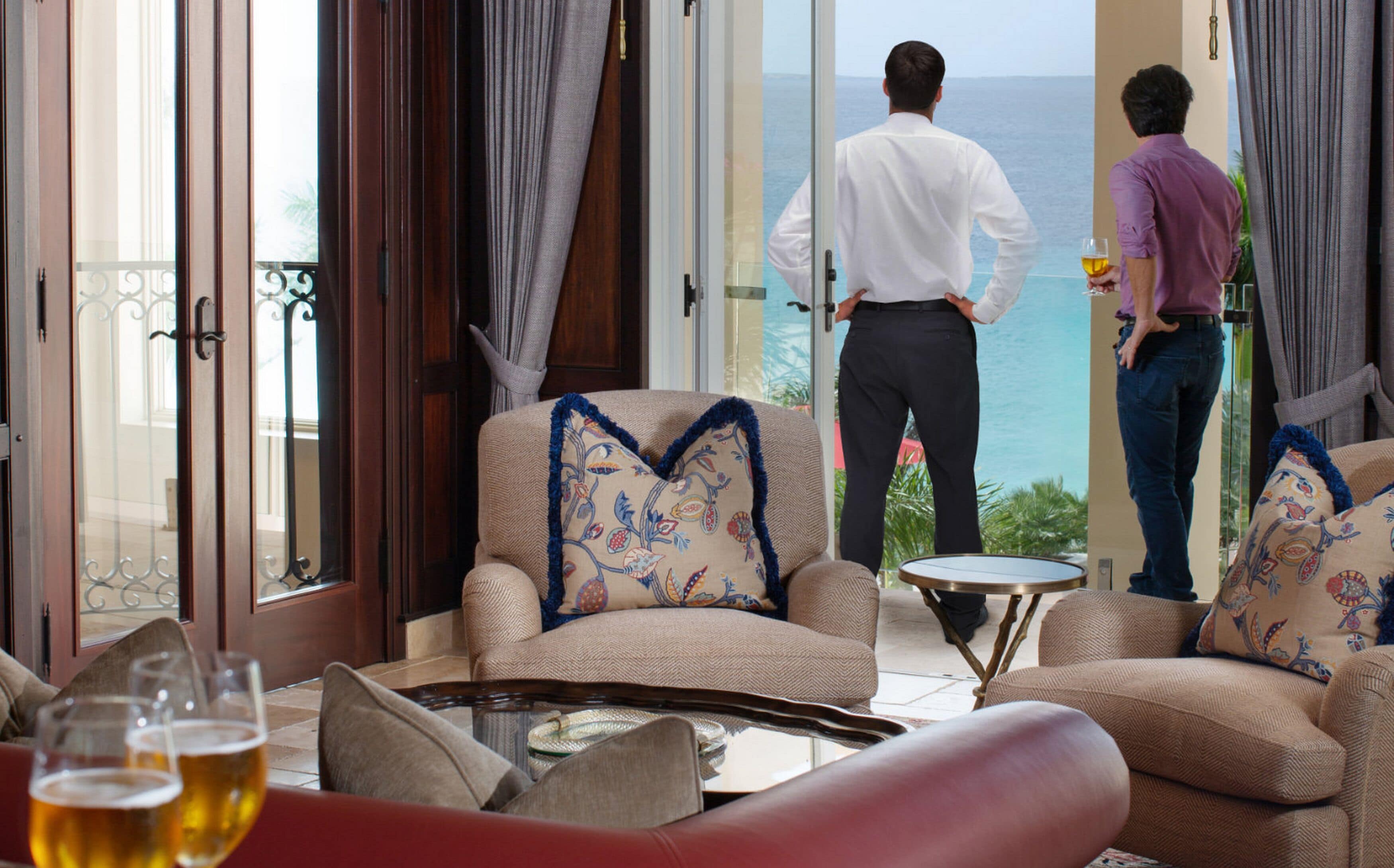A room with a view of the sea, a sofa, a coffee table, and a glass of beer.