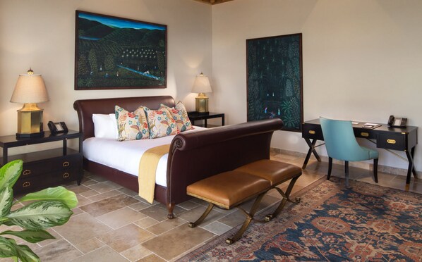A bedroom with a large bed, two bedside tables with lamps, a desk with a chair, and a large painting on the wall. - Quintessence Hotel Anguilla (West End Village)