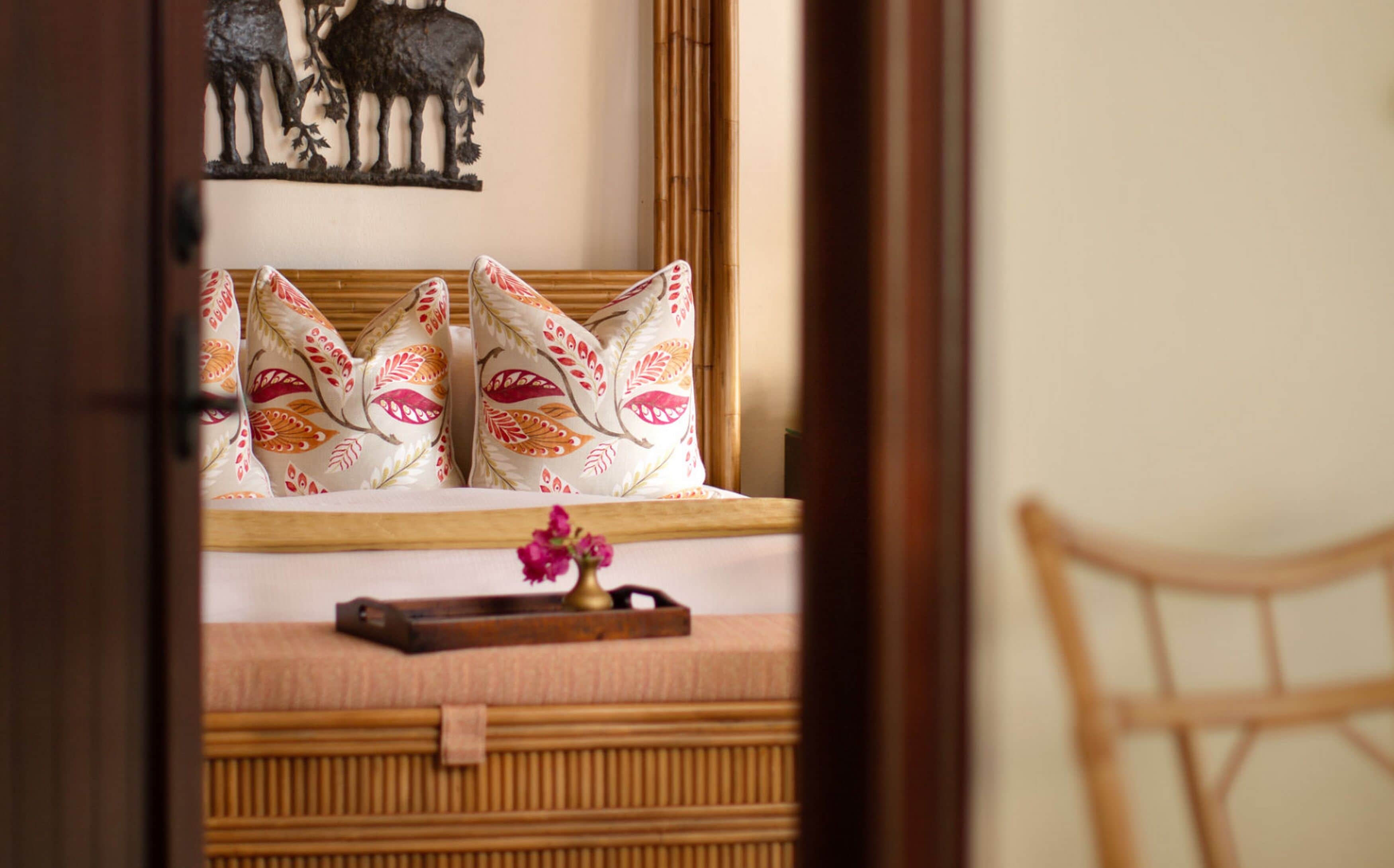 A bed with patterned pillows, a wooden headboard, and a small decorative tray with a flower.