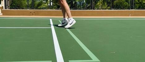 A person jumping on a tennis court with palm trees in the background.