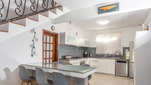 A modern kitchen with a central island, grey chairs, stainless steel appliances, and a staircase with decorative railings. - Villa with Heated Pool (Black River)