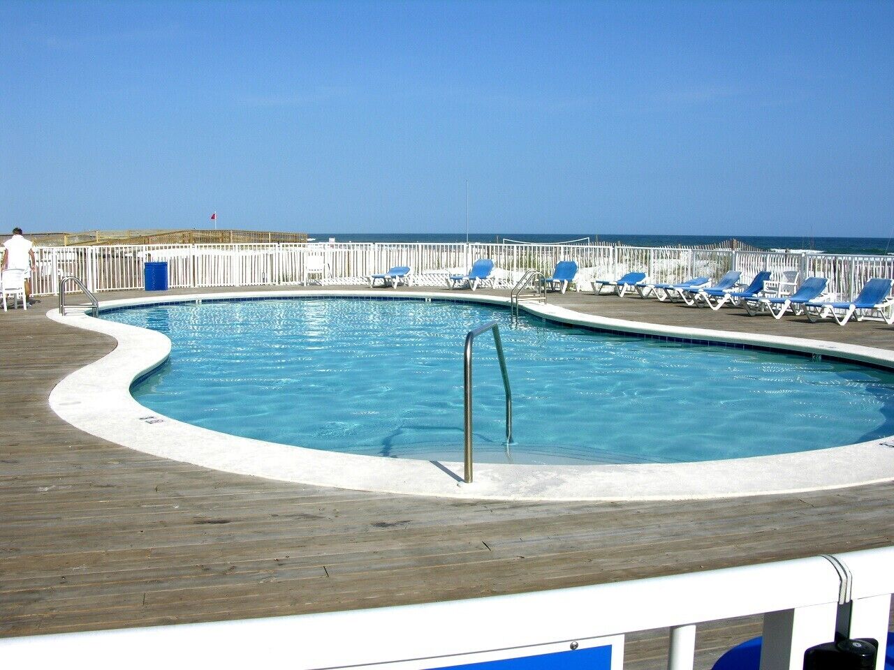 Una piscina con cubierta de madera, rodeada de sillas de descanso y una barandilla.