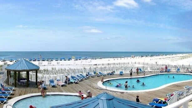 A beachside resort with multiple swimming pools, lounge chairs, and a gazebo.