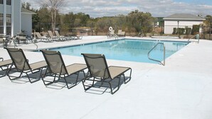 En swimmingpool med solstolar och en byggnad i bakgrunden.
