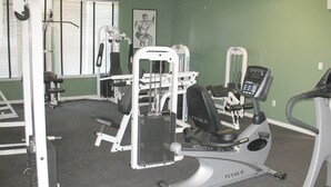 Ett gym med olika typer av träningsutrustning, inklusive ett löpband, styrketräningsmaskiner och en bänkpress.