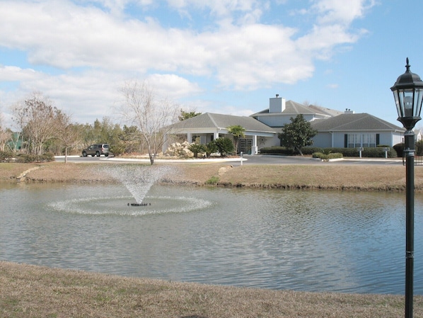 A tranquil pond with a fountain, surrounded by a well-maintained lawn and a house with a large chimney.