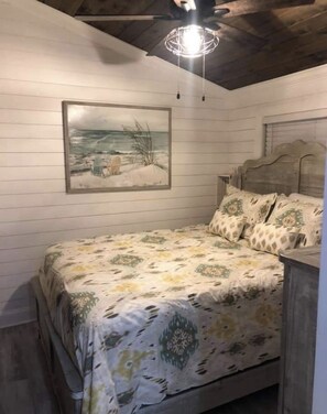 A bedroom with a bed, a headboard, a painting, and a ceiling light fixture.
