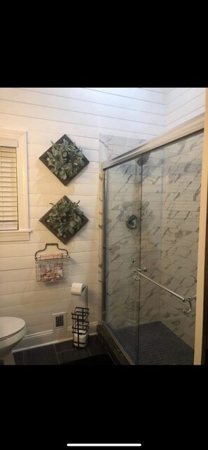 Et badeværelse med brusevæg i glas, toilet og to dekorative billeder.