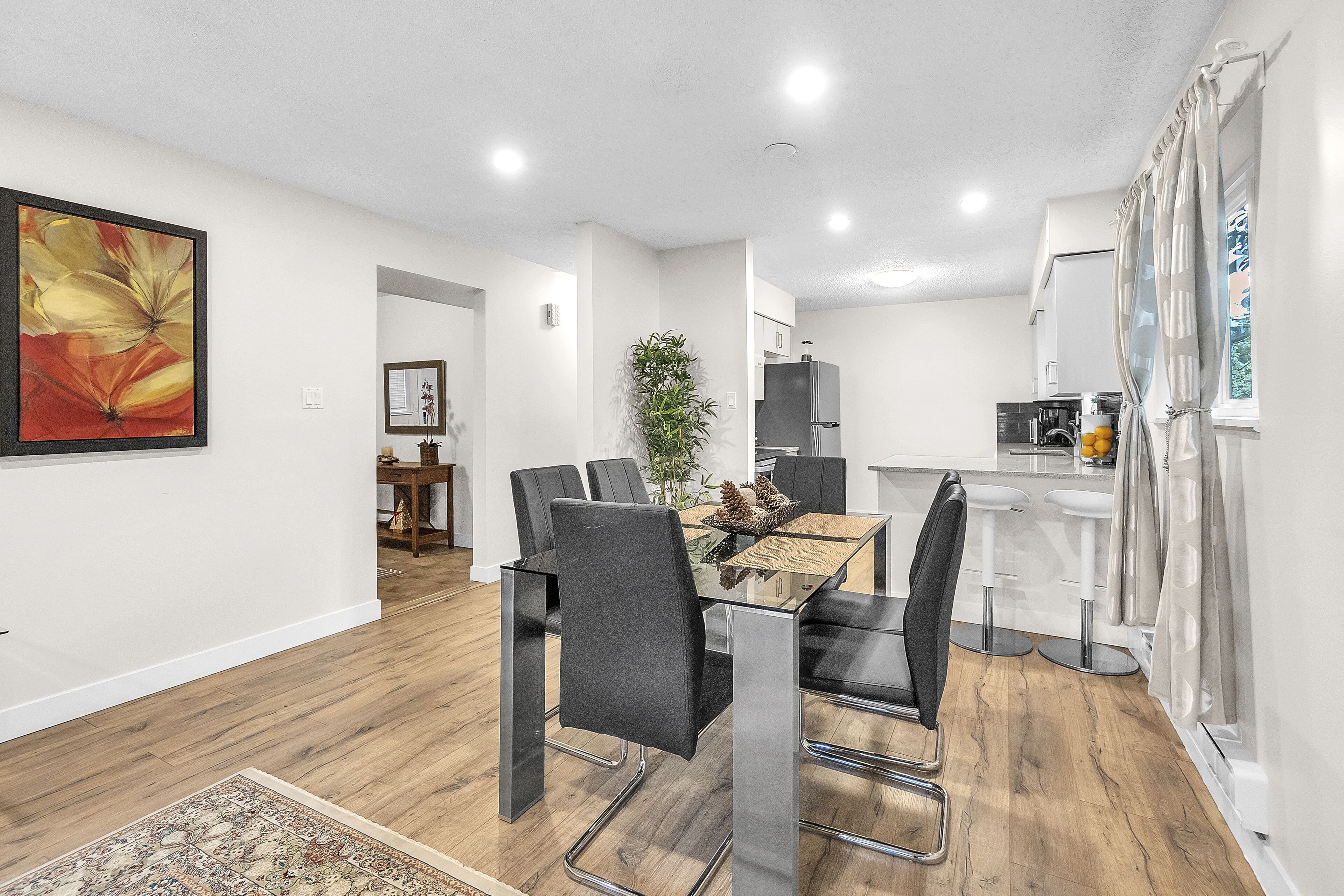 A modern kitchen with white cabinets, a black refrigerator, and a dining area with a glass table and black chairs.