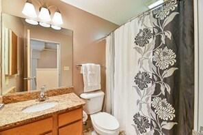 Een badkamer met een wastafel met een granieten blad, een toilet en een douchegordijn met een bloemenmotief.