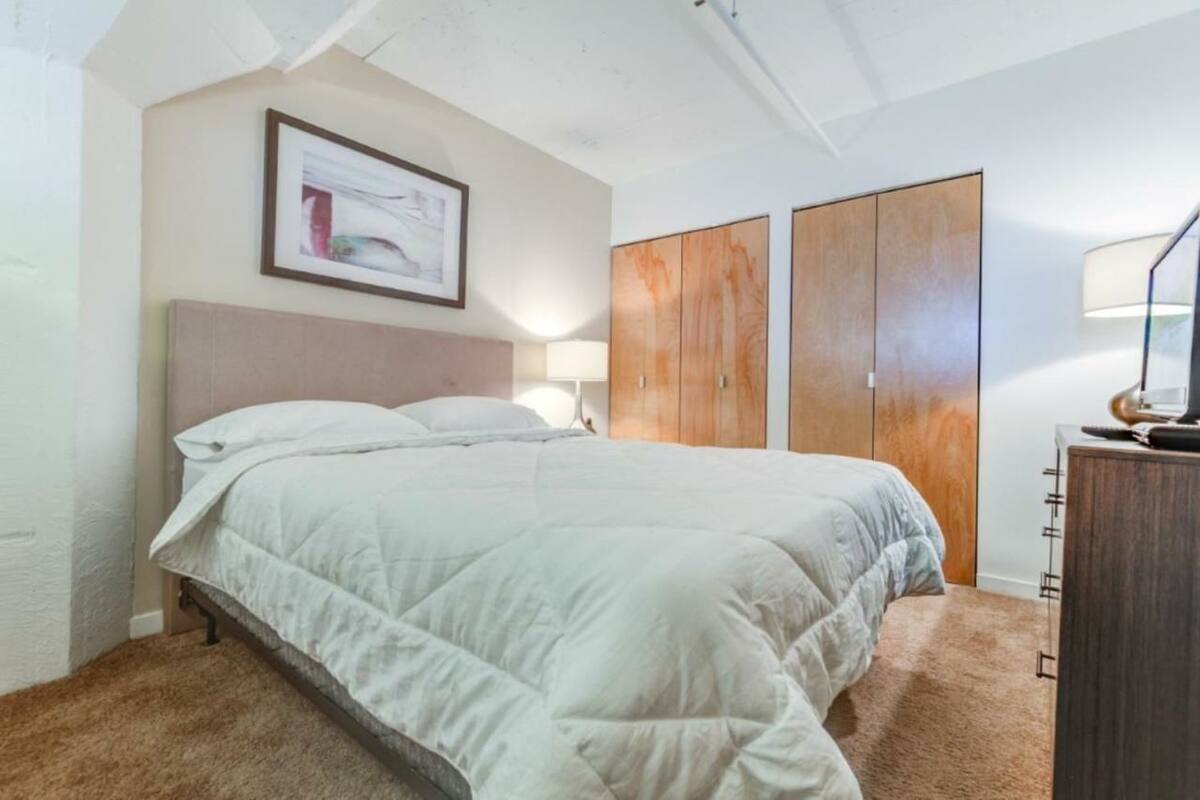 A bedroom with a bed, a wardrobe, a desk with a lamp, and a framed picture on the wall.