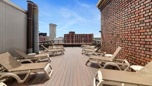 A rooftop deck with lounge chairs, a brick wall, and a view of the city skyline. - Bluebird Suites at the Warehouse District (Cleveland)