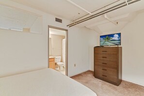 Een slaapkamer met een bed, een kapstok, een televisie en een badkamer zichtbaar door een geopende deur.