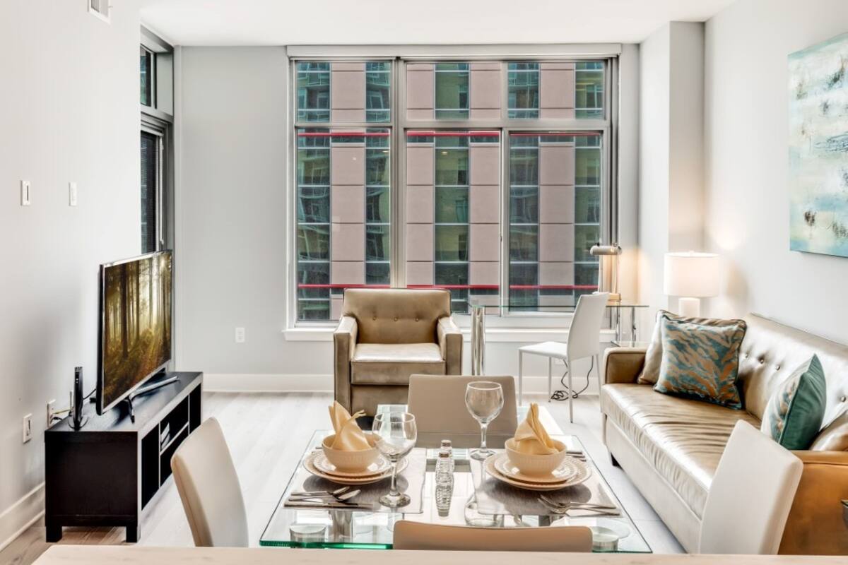 A modern living room with a glass dining table set for two, a sofa, and a television.