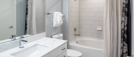 A modern bathroom with a white sink, mirror, and toilet, a shower with a curtain, and a bathtub.