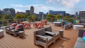 Una terraza en la azotea con mobiliario exterior, incluyendo sofás y una mesa, y vistas a la ciudad al fondo.