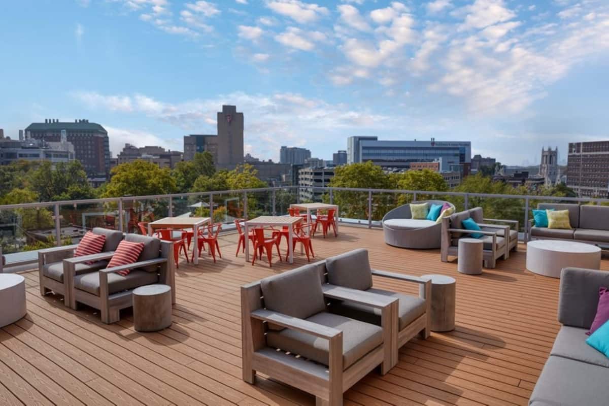 Eine Dachterrasse mit Sitzgelegenheiten im Freien, darunter Sofas und ein Tisch, sowie ein Blick auf die Stadt im Hintergrund.