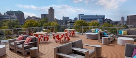 A rooftop terrace with outdoor seating, including sofas and a table, and a city view in the background.