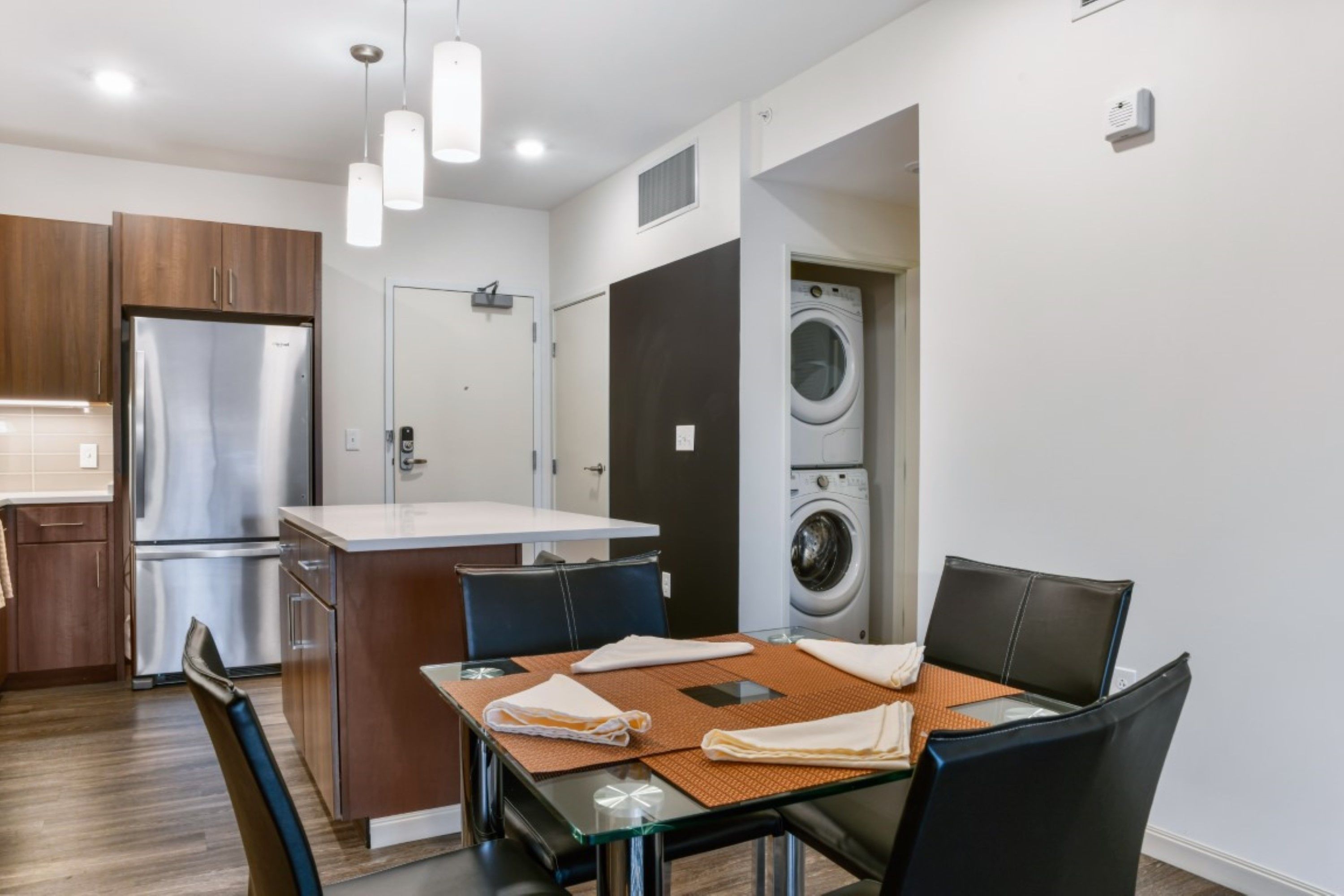 A modern kitchen with stainless steel appliances, a dining area with a glass table, and a built-in washer and dryer.