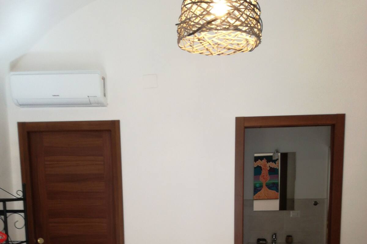 Una habitación con puerta de madera, una mesita con superficie de vidrio, un lavabo y un radiador.