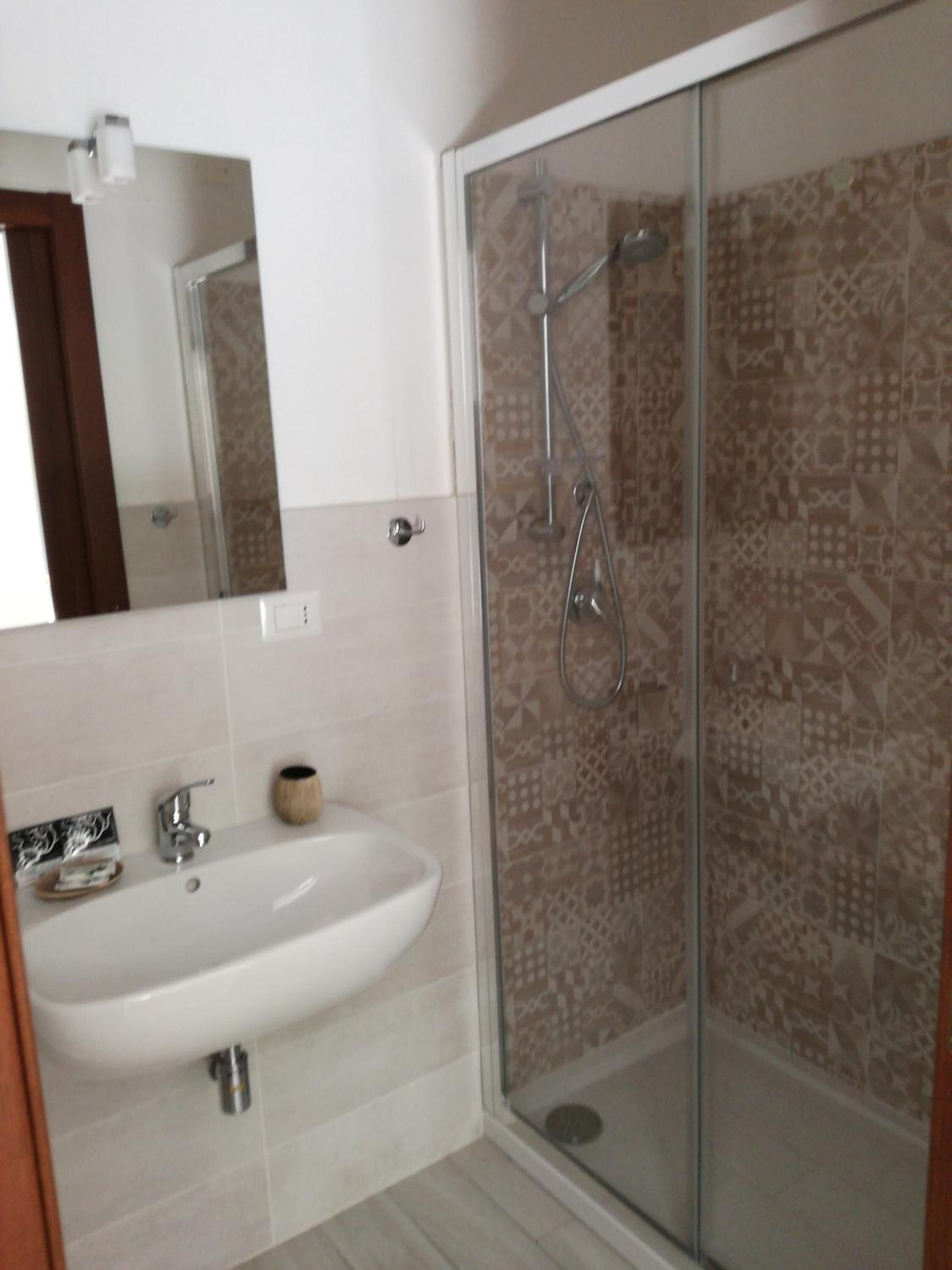 Un bany amb un lavabo blanc, un mirall i una dutxa amb envidriera de vidre i rajoles decorades.