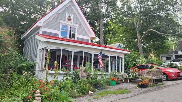 Ein Haus mit Veranda, einem kleinen Garten und einem roten Auto vor der Tür.