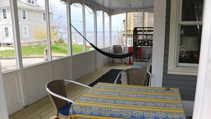 Eine überdachte Veranda mit Tisch und Stühlen, mit Blick auf eine Wohnstraße und ein Gewässer.