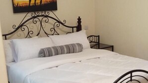 A neatly made bed with a white comforter and pillows, a metal headboard, and a painting of two people on a beach above it. - Too's Nest Edoret (Eldoret)