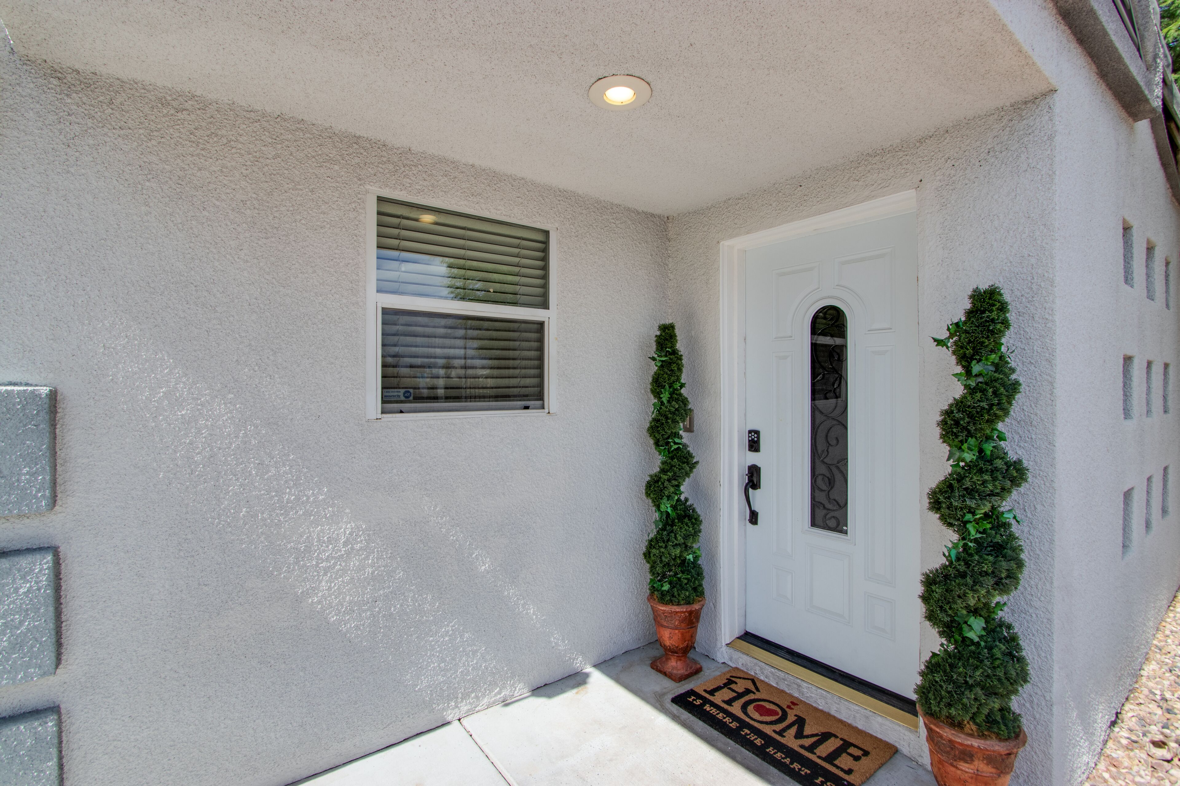 A house with a white door, a small window with blinds, and two potted plants on the porch.