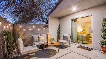 Un patio al aire libre con un conjunto de sofás, una mesa redonda y luces colgantes.