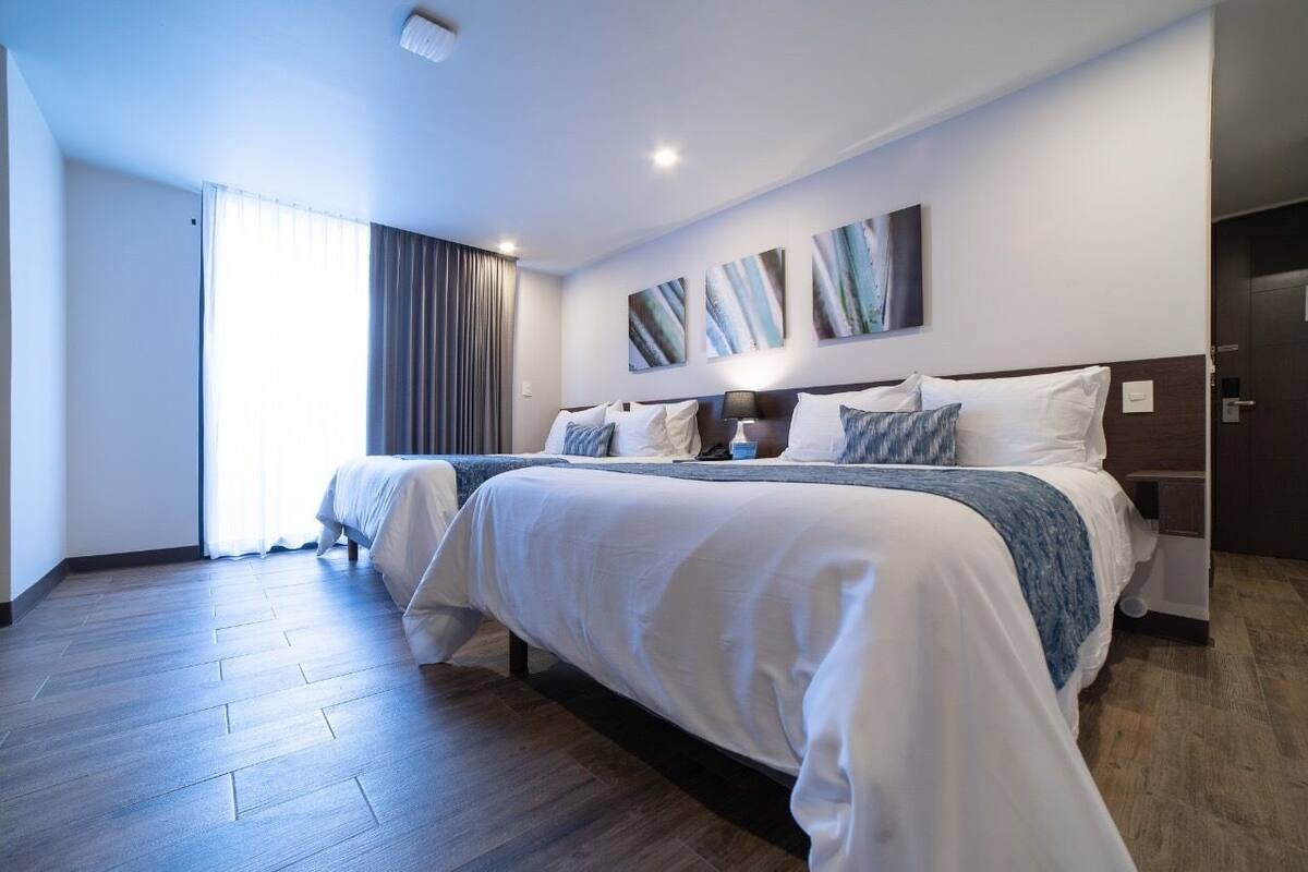 A hotel room with a large bed, a bedside table, a lamp, and a window with curtains.