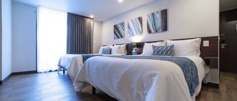 Una habitación de hotel con una cama grande, una mesita de noche, una lámpara y una ventana con cortinas.