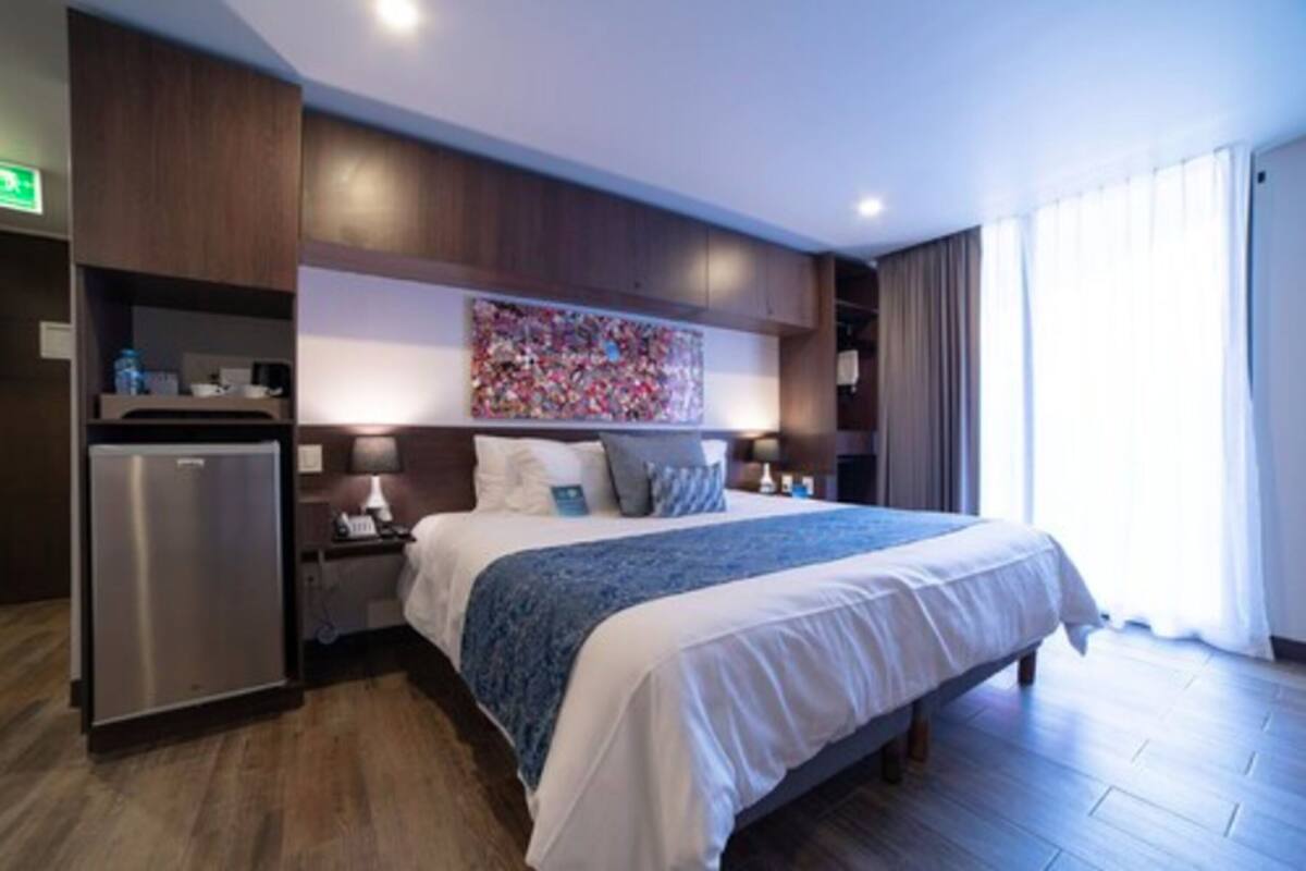 A hotel room with a bed, a desk, a refrigerator, and a large window.